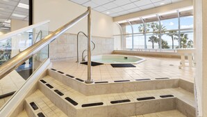 Un área de spa con un jacuzzi, escalones de mármol y barandilla de vidrio.