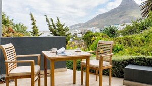 Ein Holztisch mit Stühlen auf einem Balkon mit Blick auf einen Berg und Gebäude.