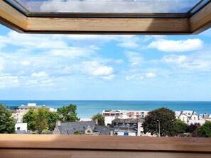 Vista da janela sobre uma vila costeira com edifícios e o mar.