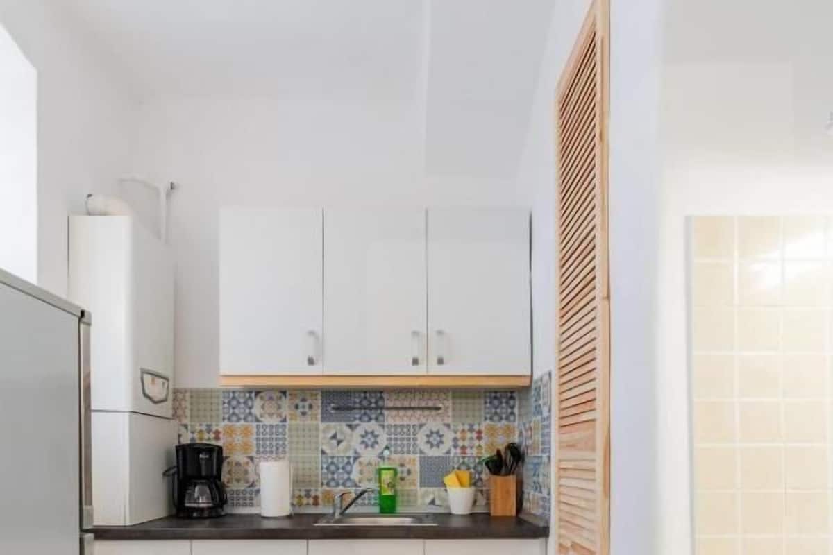 A compact kitchen with white cabinets, a tiled backsplash, and a checkered floor.