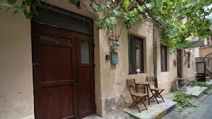 Ein Gebäude mit einer Holztür, einer kleinen Außenbereich-Sitzgelegenheit mit Tisch und Stühlen sowie einem gepflasterten Innenhof.