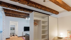 Ein Zimmer mit Holzbalkendecke, einem weißen Kleiderschrank, einem Bett mit floralem Bettzeug und einem Fernseher in der Ecke.