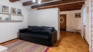 Ein Zimmer mit freiliegenden Holzbalken, einem schwarzen Ledersofa, einem farbenfrohen Streifen Teppich und einer weißen Wand mit gerahmten Bildern.