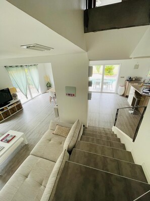 Ein modernes Interieur mit einer Treppe zu einem Balkon, einem Wohnbereich mit einer Couch und einer Küchenzeile.