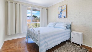 Een slaapkamer met een bed, nachtkastje, schilderij en uitzicht door een raam.