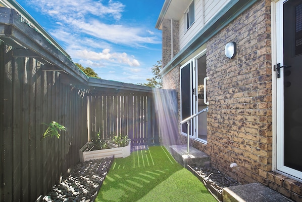 A backyard with a wooden fence, a brick wall, and a door. - Bay Breeze, 3 bedroom home (Woody Point)