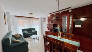 A living room with a sofa, a dining table with chairs, a TV, and a cabinet with glass doors.