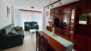 A living room with a sofa, a dining table with chairs, a TV, and a cabinet with glass doors.