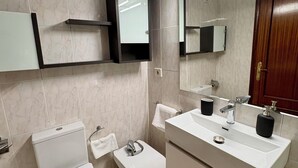 A modern bathroom with a toilet, bidet, and a sink with a mirror above.