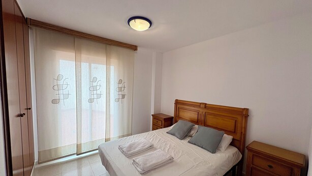 A bedroom with a bed, nightstands, a wooden headboard, a sliding door with curtains, and a ceiling light.