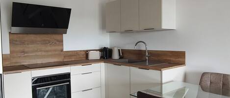 A modern kitchen with a built-in oven, a coffee maker, and a flat-screen TV mounted above the counter.