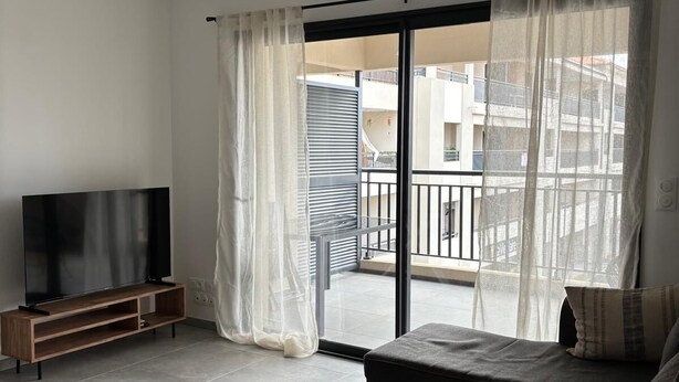 Un salón con televisor de pantalla plana, un sofá y un balcón con vistas a edificios.