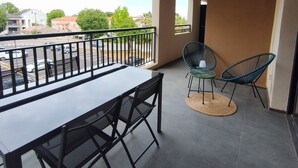 Un balcón con mesa y sillas, vista a la calle y un edificio al fondo.