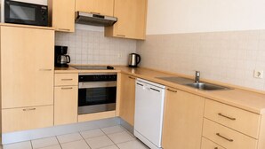 A compact kitchen with wooden cabinets, a microwave, an oven, a dishwasher, and a sink. - Vacation apartment no. 14 in Neddesitz (Neddesitz)