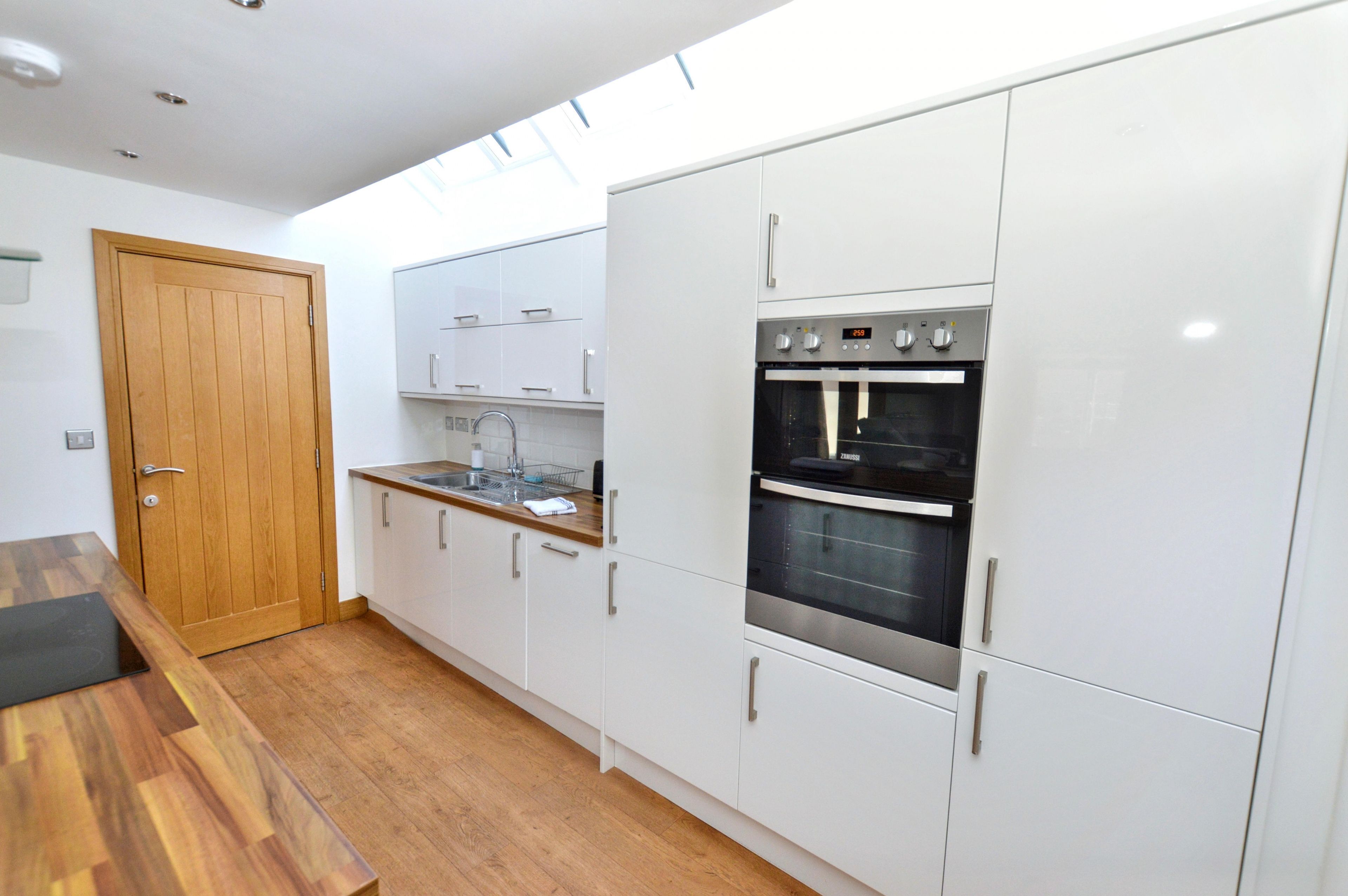 Een moderne keuken met witte kasten, een houten deur en een inbouwoven.