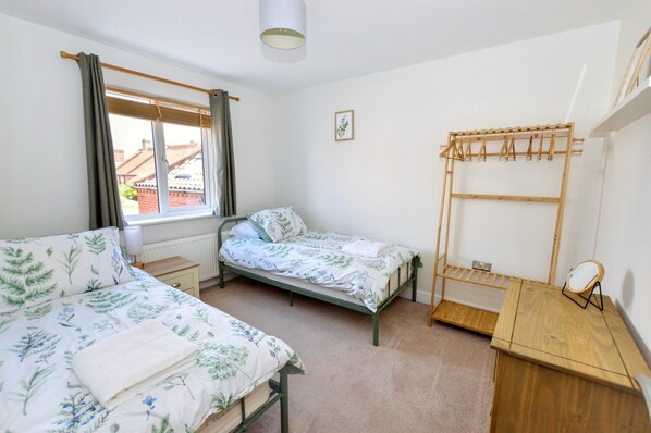 A bedroom with two single beds, a wooden desk, a hanging clothes rack, a small bedside table, and a window with curtains. - The Hideaway, Sheringham, close to shops and beach - perfect for relaxing break (Sheringham)