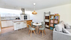 Eine moderne Küche mit weißen Schränken, ein Essbereich mit rundem Tisch und vier Stühlen sowie ein graues Sofa in einem Wohnbereich.