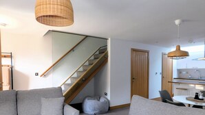 Ein modernes Wohnzimmer mit Treppe, grauen Sofas, einem Sitzsack und einer Küchenzeile.