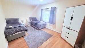 A bedroom with two beds, a wardrobe, a window with curtains, and a small rug. - House In Cannock-3 Bed Sleeps 5 (Cannock)