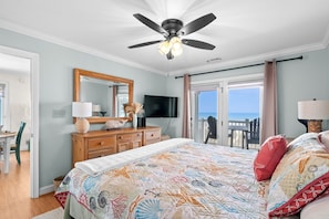 Ein Schlafzimmer mit Bett, Deckenventilator, Fernseher, Kommode, Schreibtisch und einem Balkon mit Blick.
