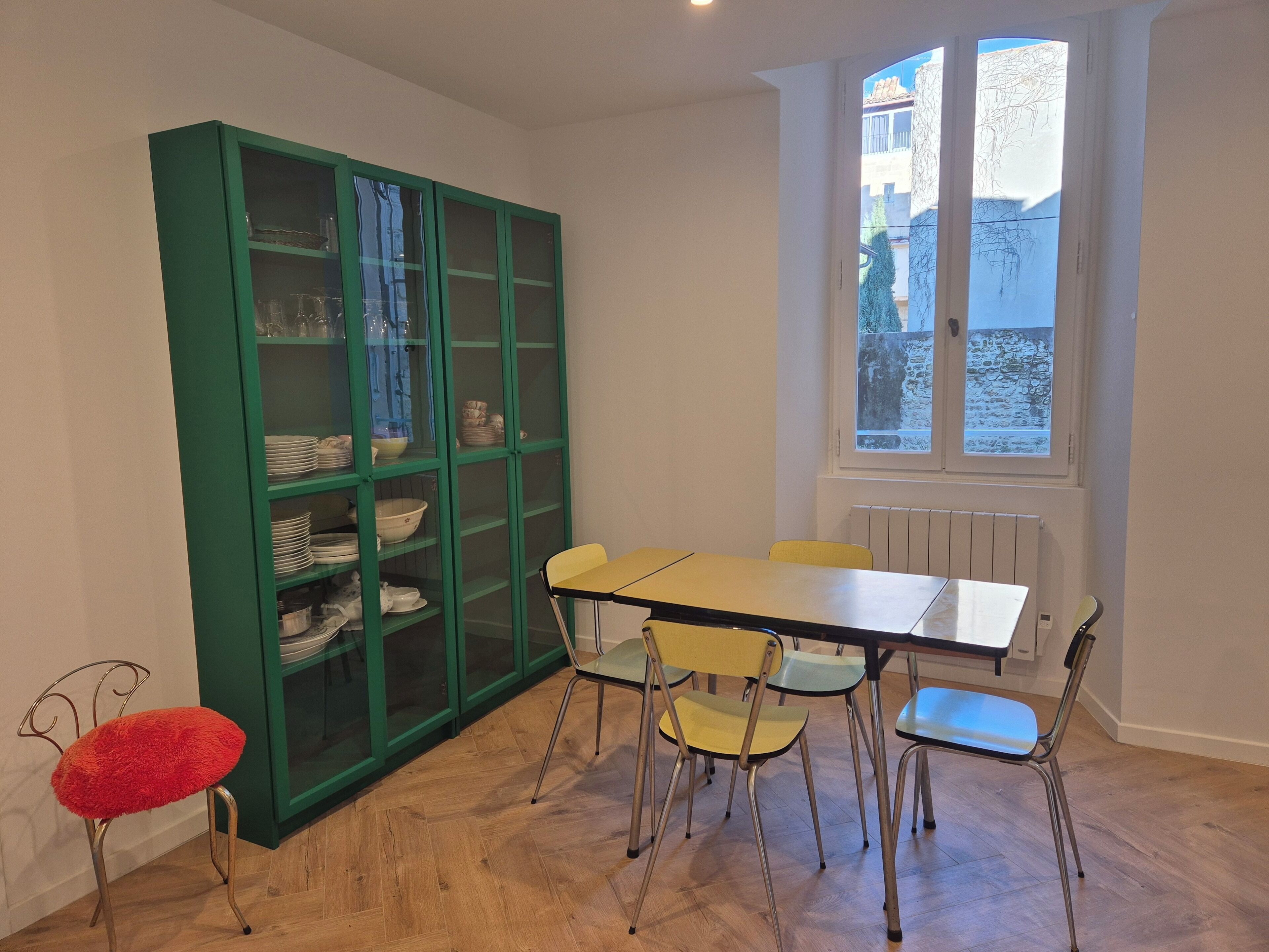 Een eetgedeelte met een tafel, stoelen, een groene kast met glazen deuren en een raam met uitzicht.