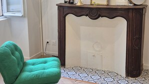 Una habitación con un sillón verde, suelo de madera, chimenea y un espejo sobre una consola de madera.