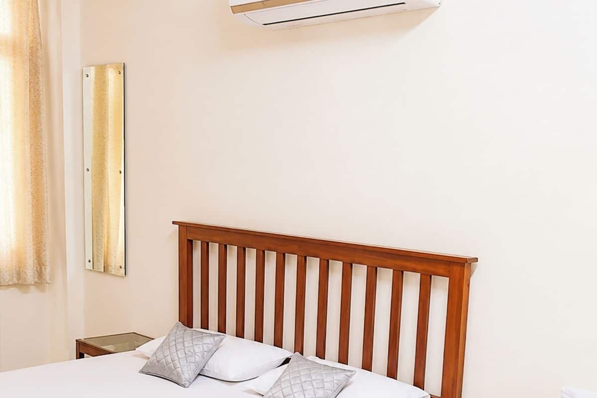 A hotel room with two beds, a wooden headboard, a bedside table with a glass, and an air conditioning unit on the wall.