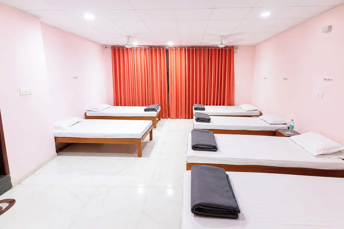 A hotel room with four single beds, a ceiling fan, and a window with orange curtains.