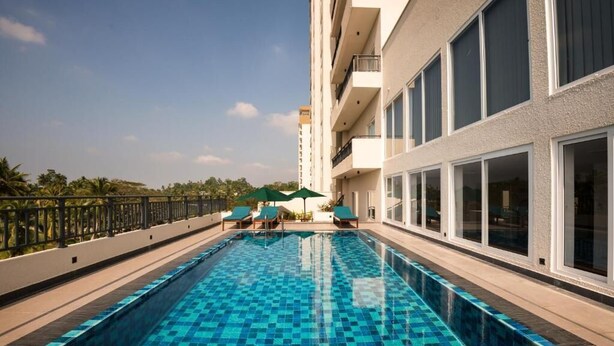 A swimming pool with a checkered pattern, surrounded by lounge chairs and umbrellas, adjacent to a building with large windows and balconies. - Elegant 3BR Apartment Near Galle Fort & Beach (Galle)