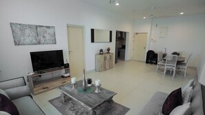 A living room with a sofa, a coffee table, a TV, and a dining area with chairs and a table. - Elegant 3BR Apartment Near Galle Fort & Beach (Galle)