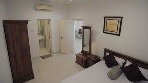 A bedroom with a bed, a dresser, a mirror, and a door leading to a bathroom. - Elegant 3BR Apartment Near Galle Fort & Beach (Galle)