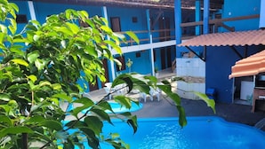 A swimming pool with a blue deck, surrounded by a building with blue walls and a tiled roof. - HOTEL LAGOA AZUL (Porto Seguro)