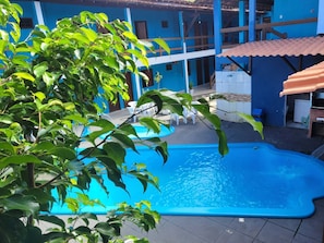 A swimming pool with a blue deck, surrounded by a building with blue walls and a tiled roof. - HOTEL LAGOA AZUL (Porto Seguro)