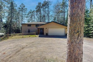 A two-story building with a garage, surrounded by trees. - Waterfront, dog-friendly home with dock, kayaks, NEW hot tub, game room, & AC (Eagle River)