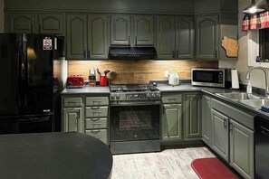 A kitchen with green cabinets, a black refrigerator, a red toaster, a microwave, and a stove. - Waterfront, dog-friendly home with dock, kayaks, NEW hot tub, game room, & AC (Eagle River)