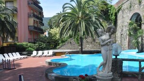 A swimming pool with a statue, lounge chairs, and a building with balconies. - Hotel Residence Moneglia (Moneglia)