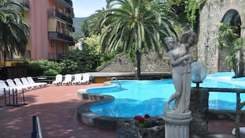 Una piscina con una statua, sdraio e un edificio con balconi.