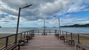 Un muelle de madera con bancos, un farol y vistas al mar y colinas distantes.