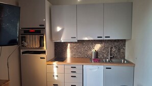 A compact kitchen with white cabinets, a built-in oven, a dishwasher, and a tiled backsplash.