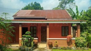 Uma casa de dois andares com telhado vermelho, varanda frontal e um pequeno jardim.