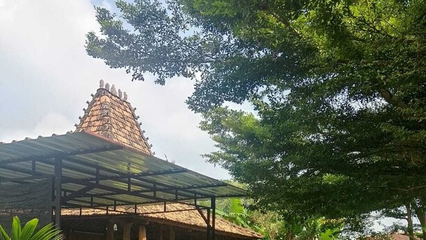 Um edifício tradicional com telhado de palha, rodeado por um jardim bem cuidado com diversas plantas e um caminho pavimentado.
