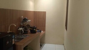 Uma cozinha compacta com geladeira, pia e bancada. Há armários acima da bancada e uma janela na parede da direita.
