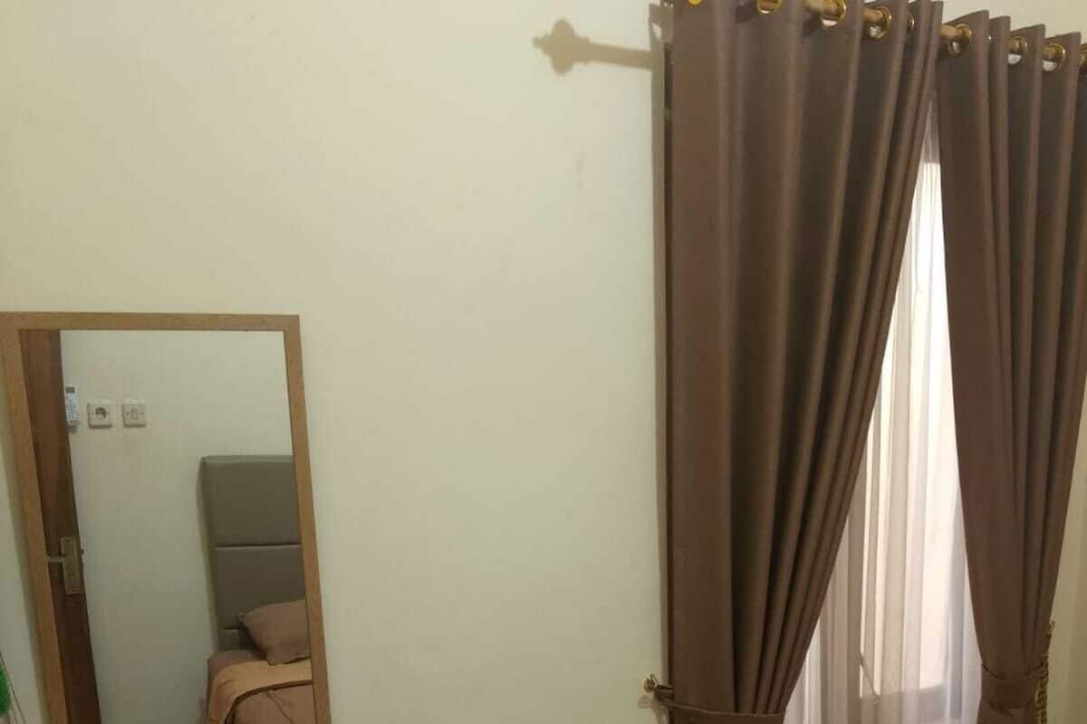 A bedroom with a bed, a bedside table with a mirror, and a window with curtains.