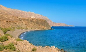 A coastal landscape with a building on a cliff, a beach, and clear blue sea.