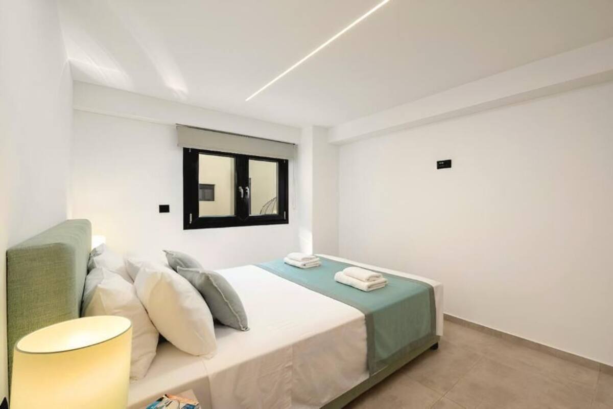 A modern hotel room with a bed, a bedside lamp, a window, and a mirror.