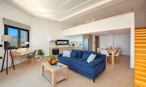 A modern living room with a blue sofa, a wooden desk, and a dining area with a table and chairs.