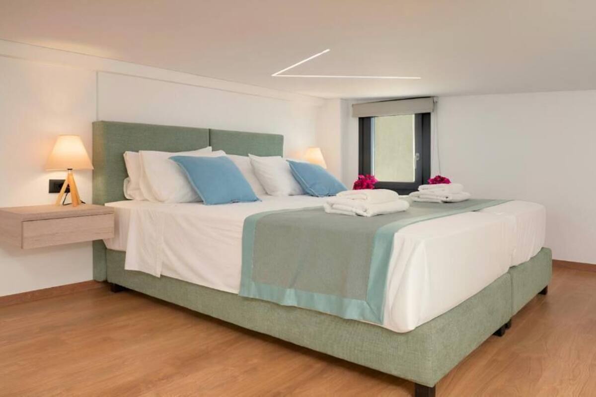 A modern hotel room with a bed, bedside lamps, a window, and a wooden floor.