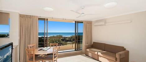 A modern living room with a balcony, a sofa, a dining table with chairs, and a TV.