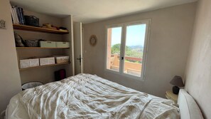 Ein Schlafzimmer mit Bett, Fenster mit Blick, Nachttisch mit Lampe und Regalen mit Aufbewahrungsboxen.