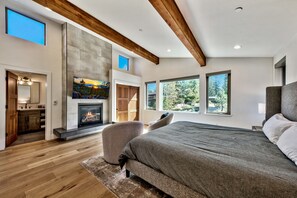 A modern bedroom with a fireplace, large windows, and a wooden ceiling.